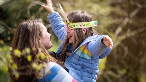 A young mum lifting her daughter, who is wearing paper bunny ears, into her arms at a National Trust property